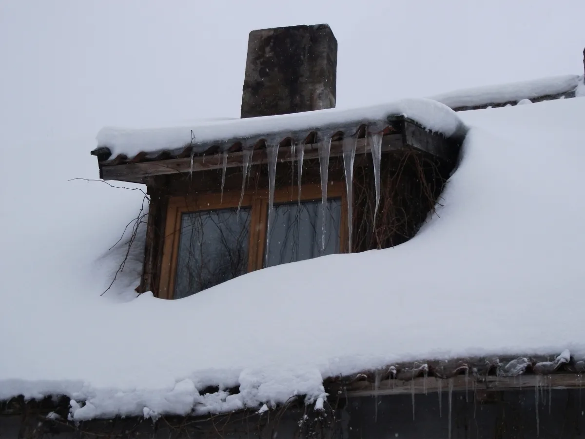 Snow-buried dormer window lined with icicles
